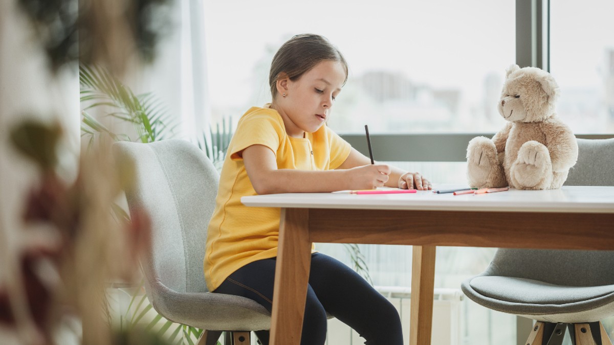 Young girl studying and writing at a desk by a window